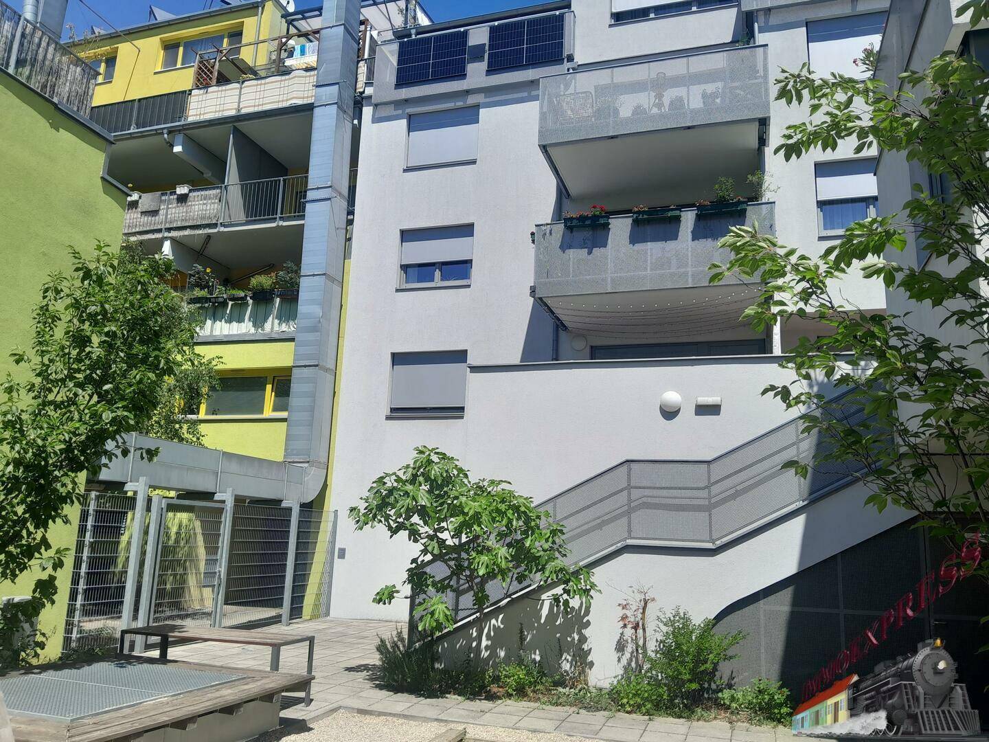 Moderne Gebäudefassade mit Balkonen, Photovoltaikanlage und begrüntem Innenhof.