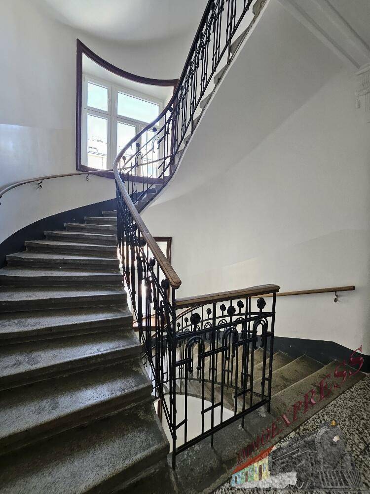 Weitläufiges Treppenhaus mit geschwungenem Geländer und großen Fenstern, typisch für Altbauten.