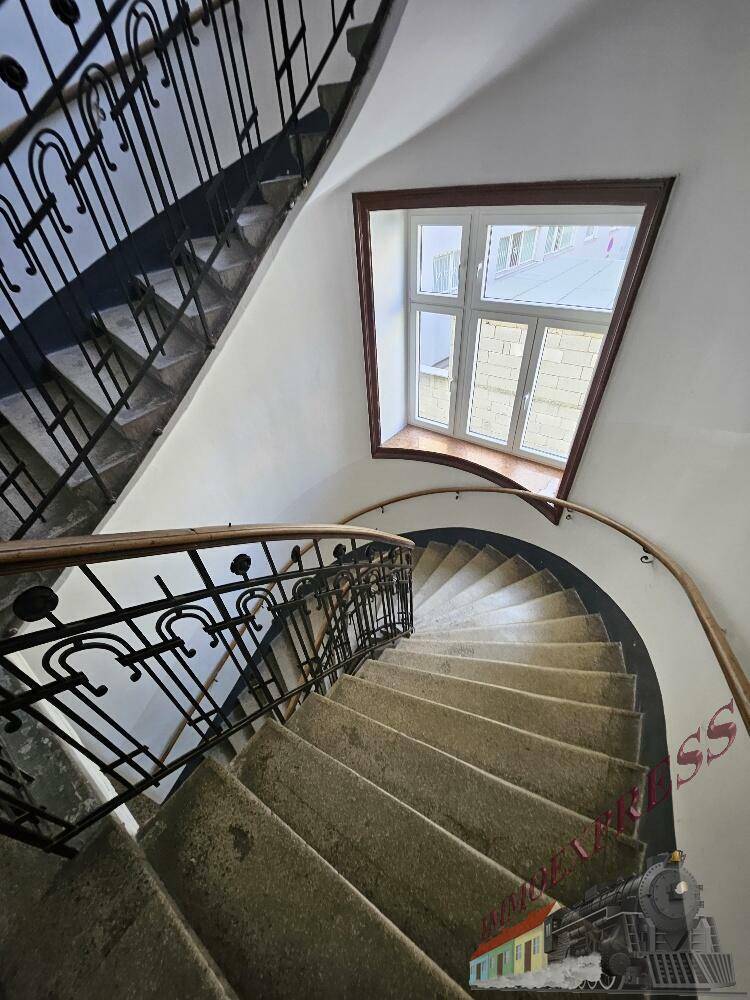 Elegantes Wendeltreppenhaus mit kunstvollem Geländer und natürlichem Lichteinfall durch ein Fenster.