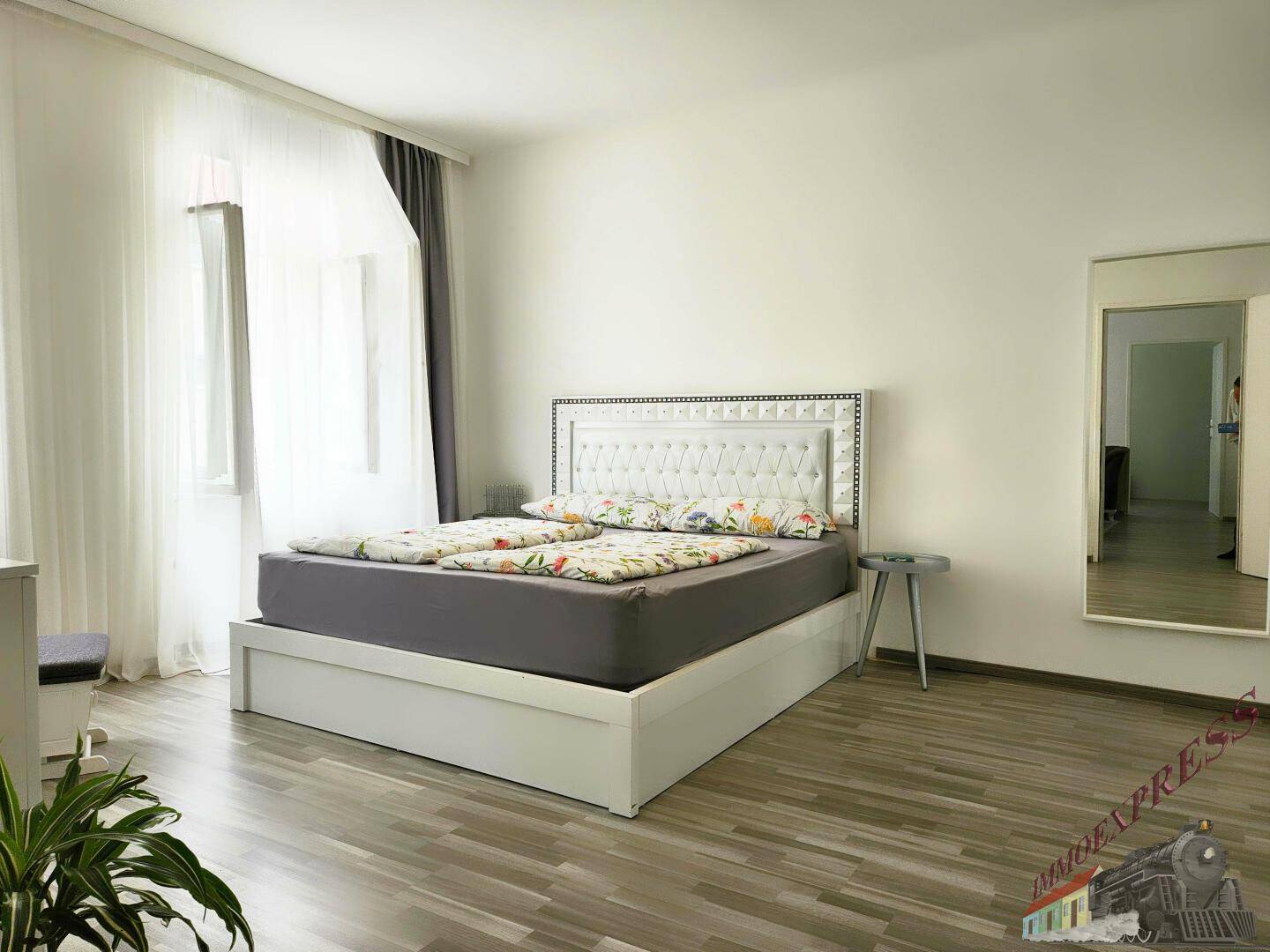 Geräumiges Schlafzimmer mit modernem Doppelbett, Laminatboden und großen Fenstern.