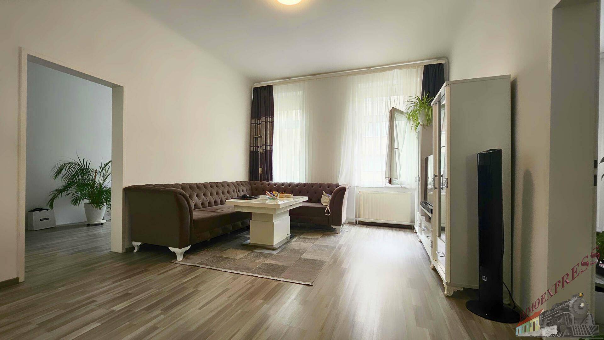 Helles Wohnzimmer mit bequemer Couch, Holzboden und Blick nach draußen.