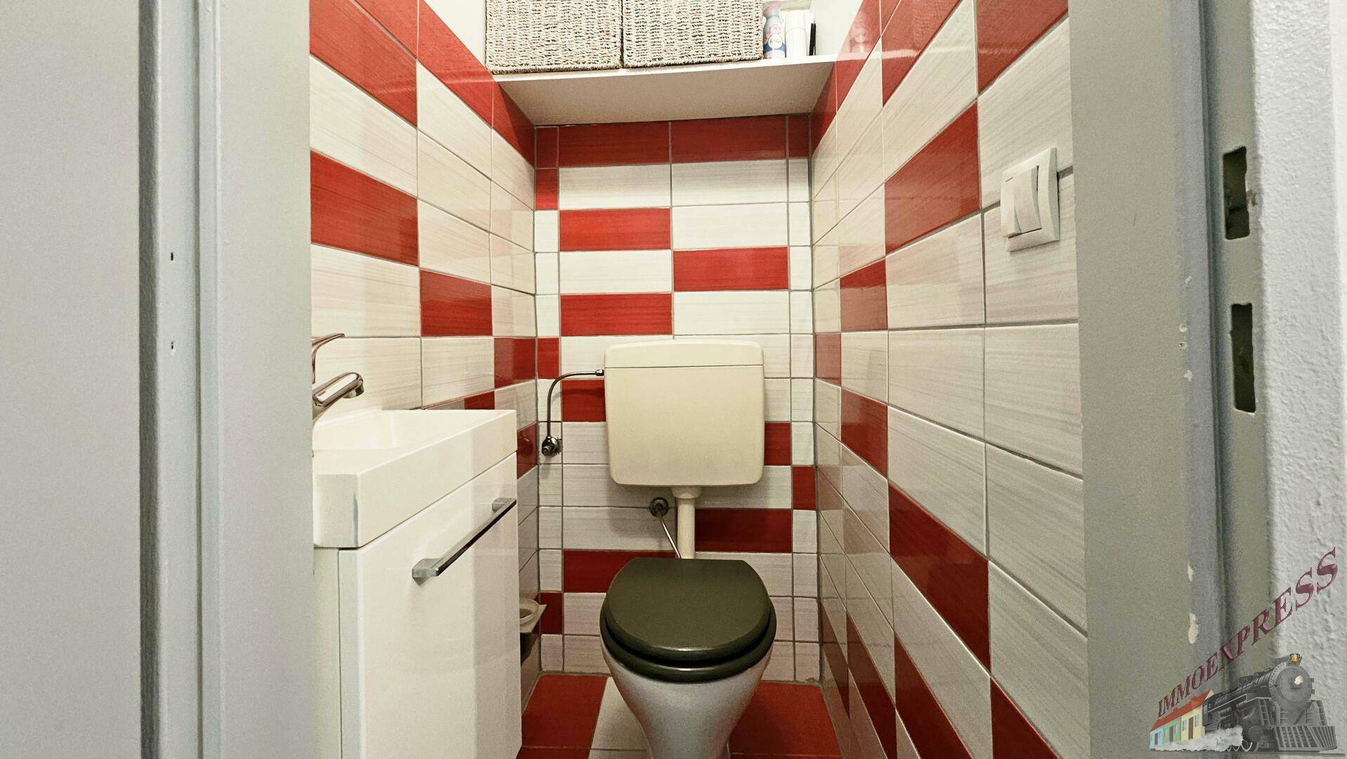 Kleines Gäste-WC mit auffälligen rot-weißen Fliesen und modernem Waschbecken.
