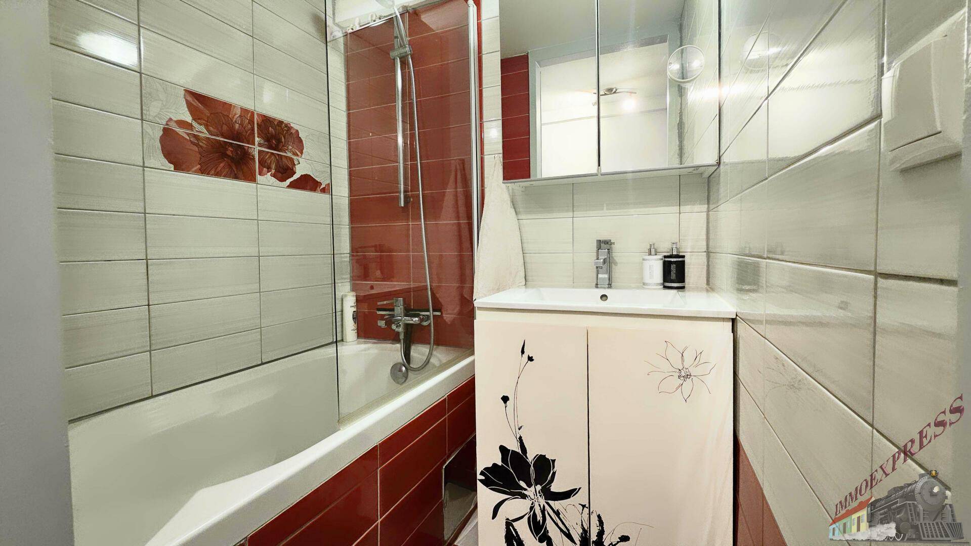 Badezimmer mit Badewanne, Duschfunktion und rot-weißen Fliesen, inklusive Spiegelschrank.