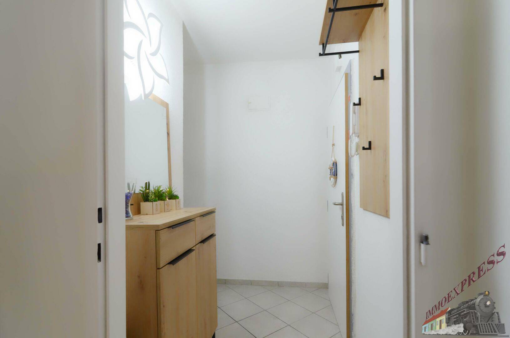 Heller Eingangsbereich mit praktischem Schuhschrank, Spiegel und Garderobe auf weiß gefliestem Boden.