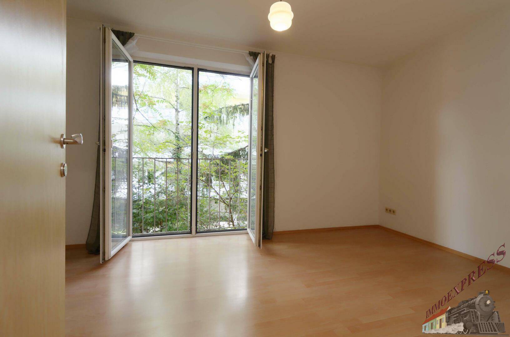 Lichtdurchflutetes Zimmer mit Holzfußboden und weit geöffneten Balkontüren mit Blick ins Grüne.