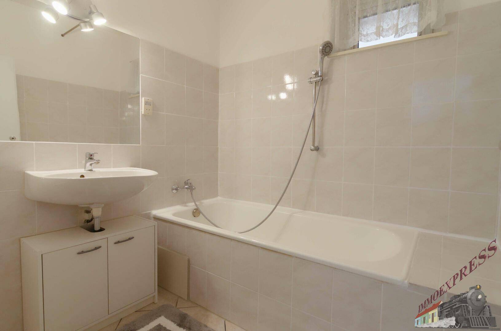 Gefliestes Badezimmer mit Badewanne, Waschbecken, großem Spiegel und Fenster für Tageslicht.