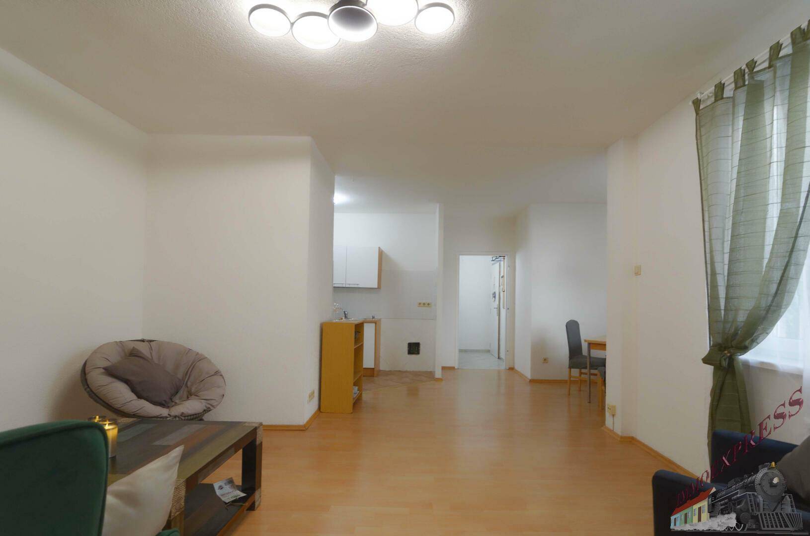 Offener Wohnbereich mit Verbindung zur Küche und Flur, ausgestattet mit hellem Holzfußboden.