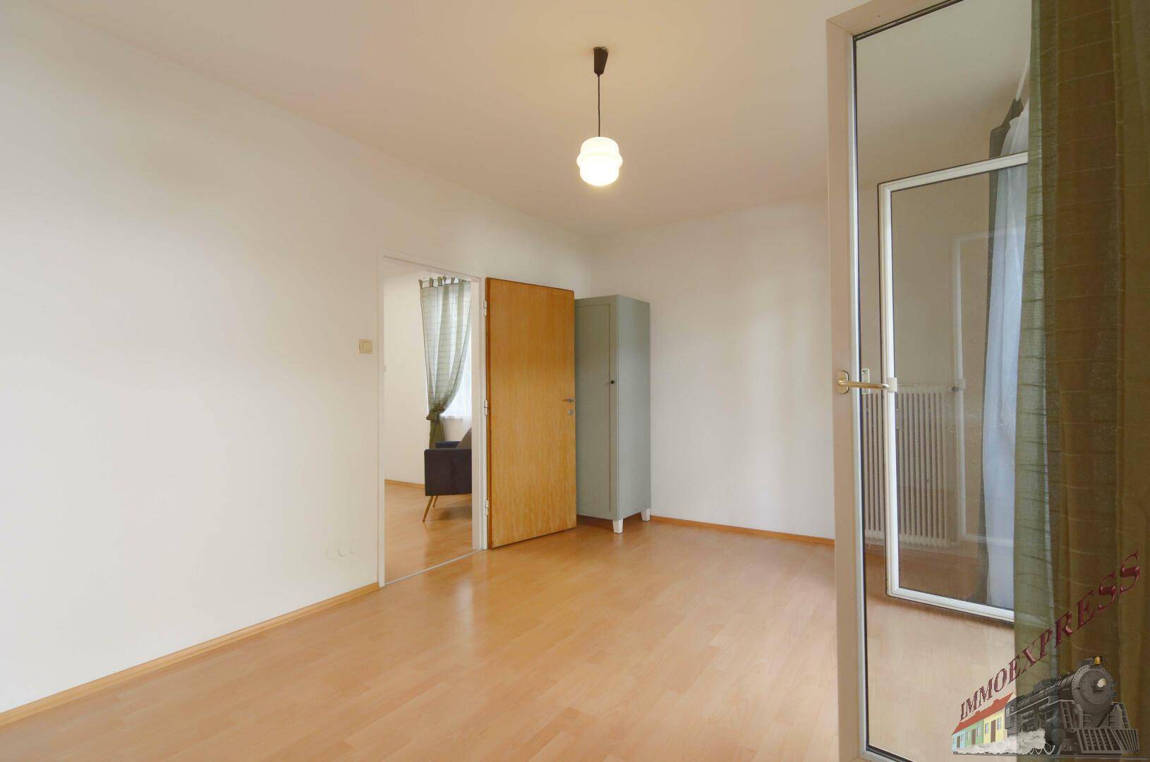 Helles Zimmer mit Holzfußboden und Zugang zu einem Balkon, ideal als Schlaf- oder Arbeitszimmer.