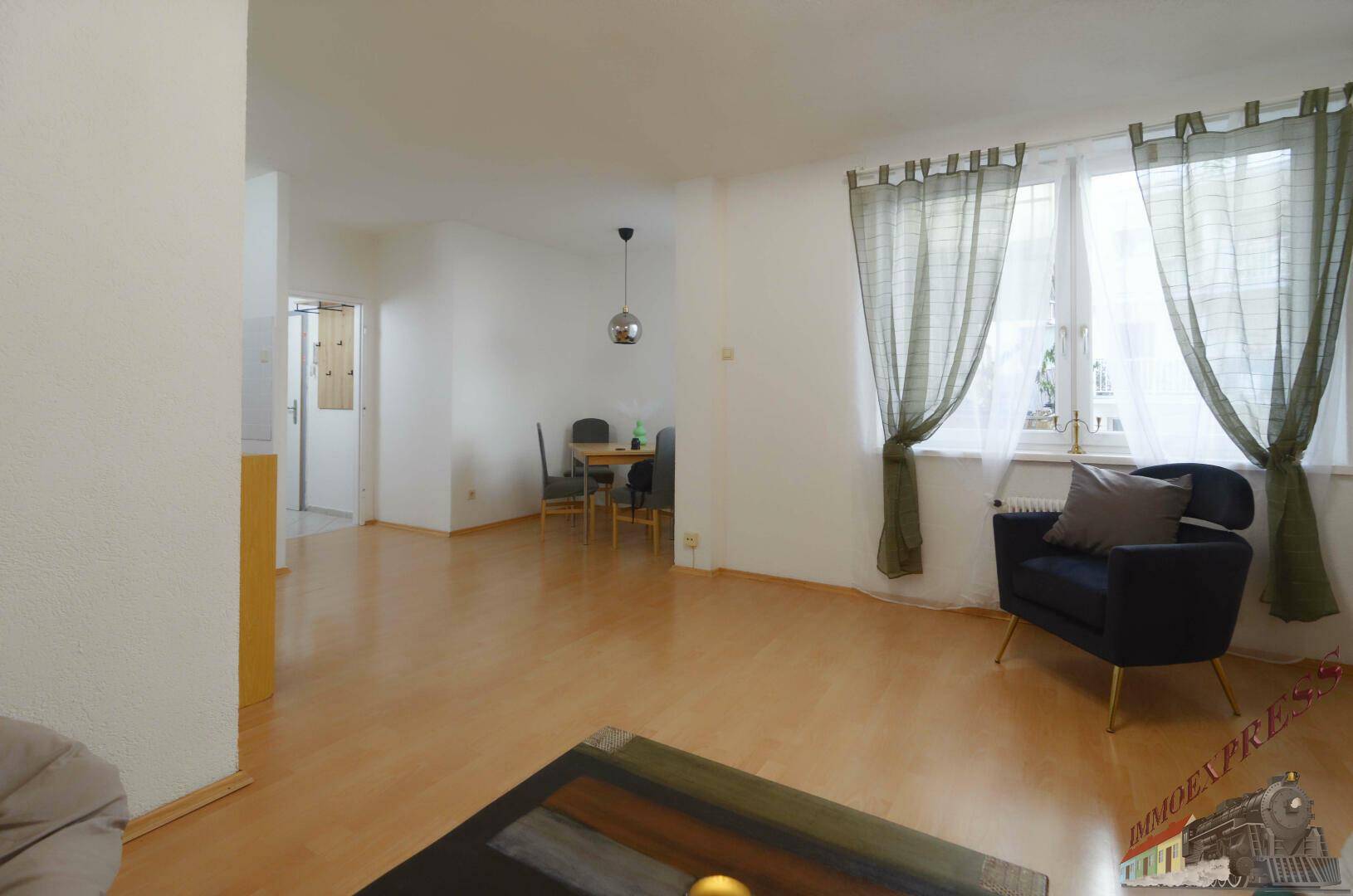 Geräumiger Wohn-Essbereich mit hellem Holzfußboden und Fenster mit grünen Vorhängen.