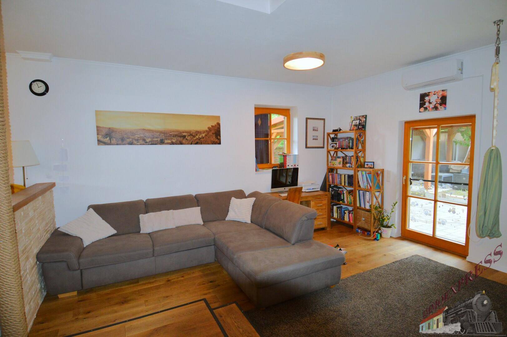 Heller Wohnbereich mit Ecksofa, Schreibtisch und Blick in den Garten, perfekt für Home-Office.