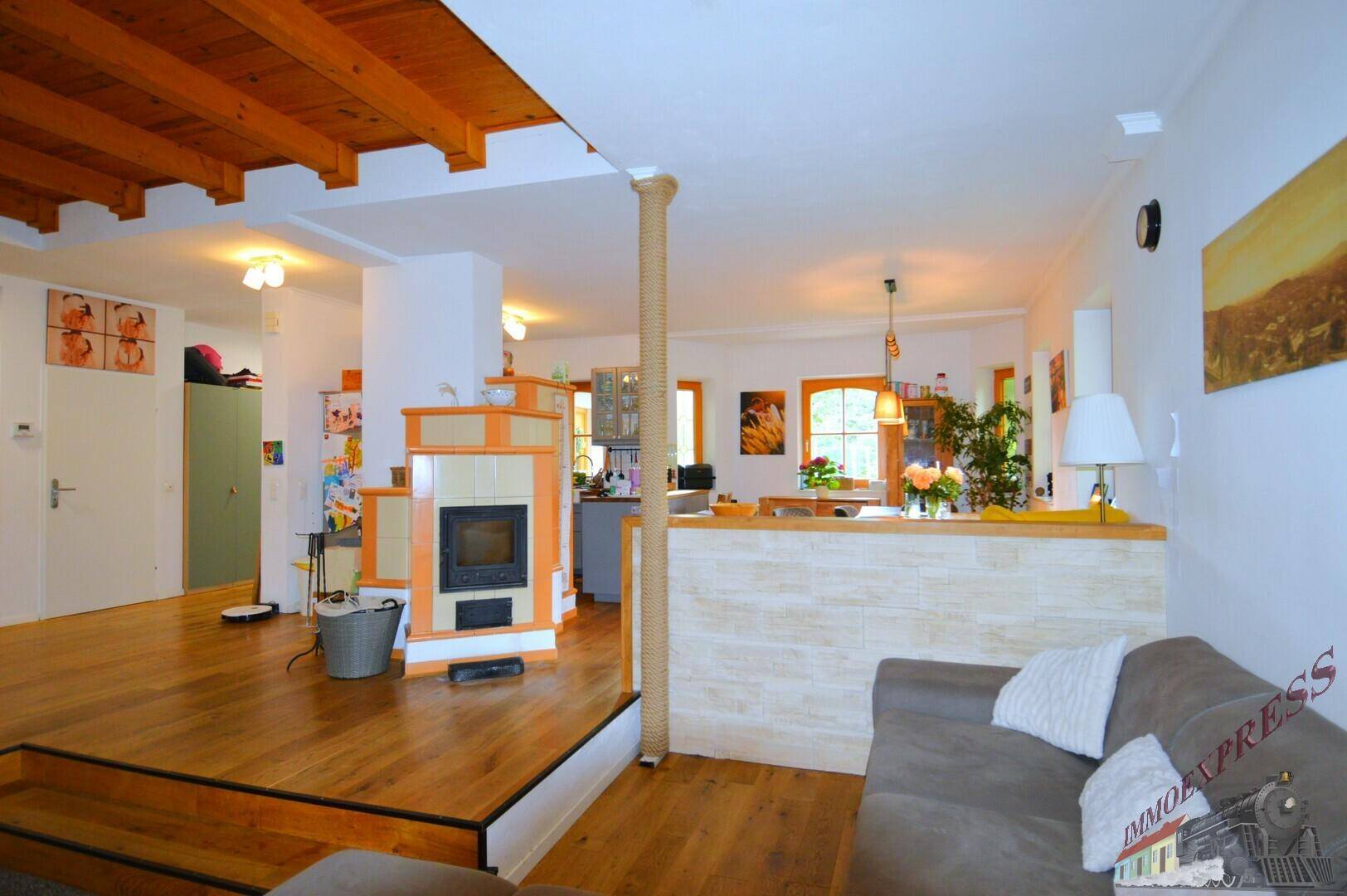 Helles Wohnzimmer mit Holzboden, traditionellem Kachelofen und sichtbaren Holzdeckenbalken, offen gestaltet.