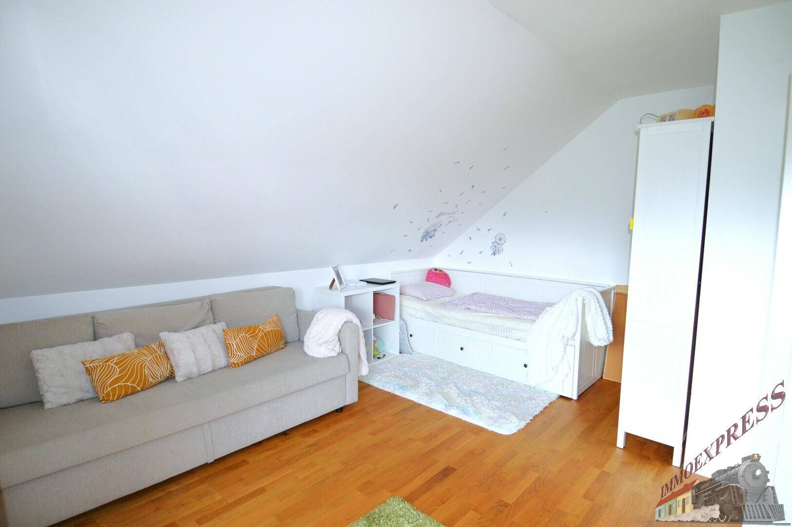 Helles Schlafzimmer im Dachgeschoss mit Sofa, Bett und Holzboden, ideal für Kinder.