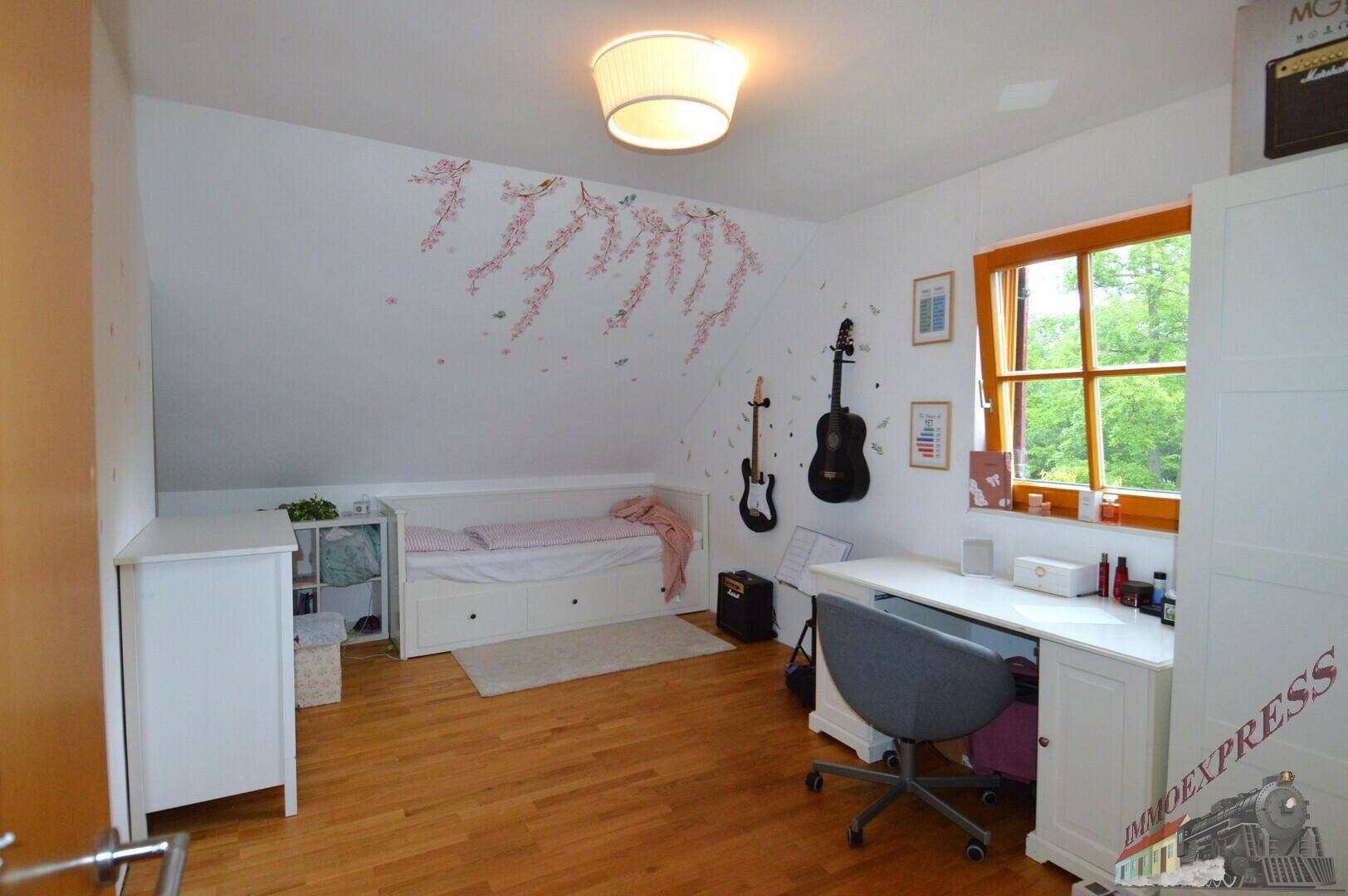 Freundliches Kinderzimmer im Dachgeschoss mit Bett, Schreibtisch und Holzboden.