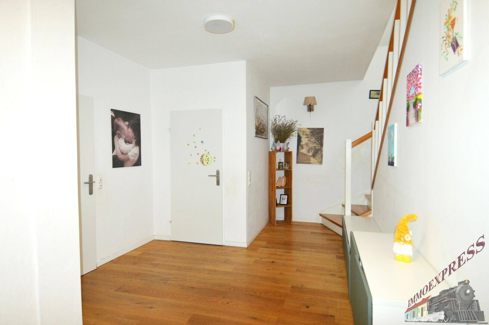 Heller Flur mit Holztreppe zum Obergeschoss und schlichten weißen Wänden, gut gepflegt.