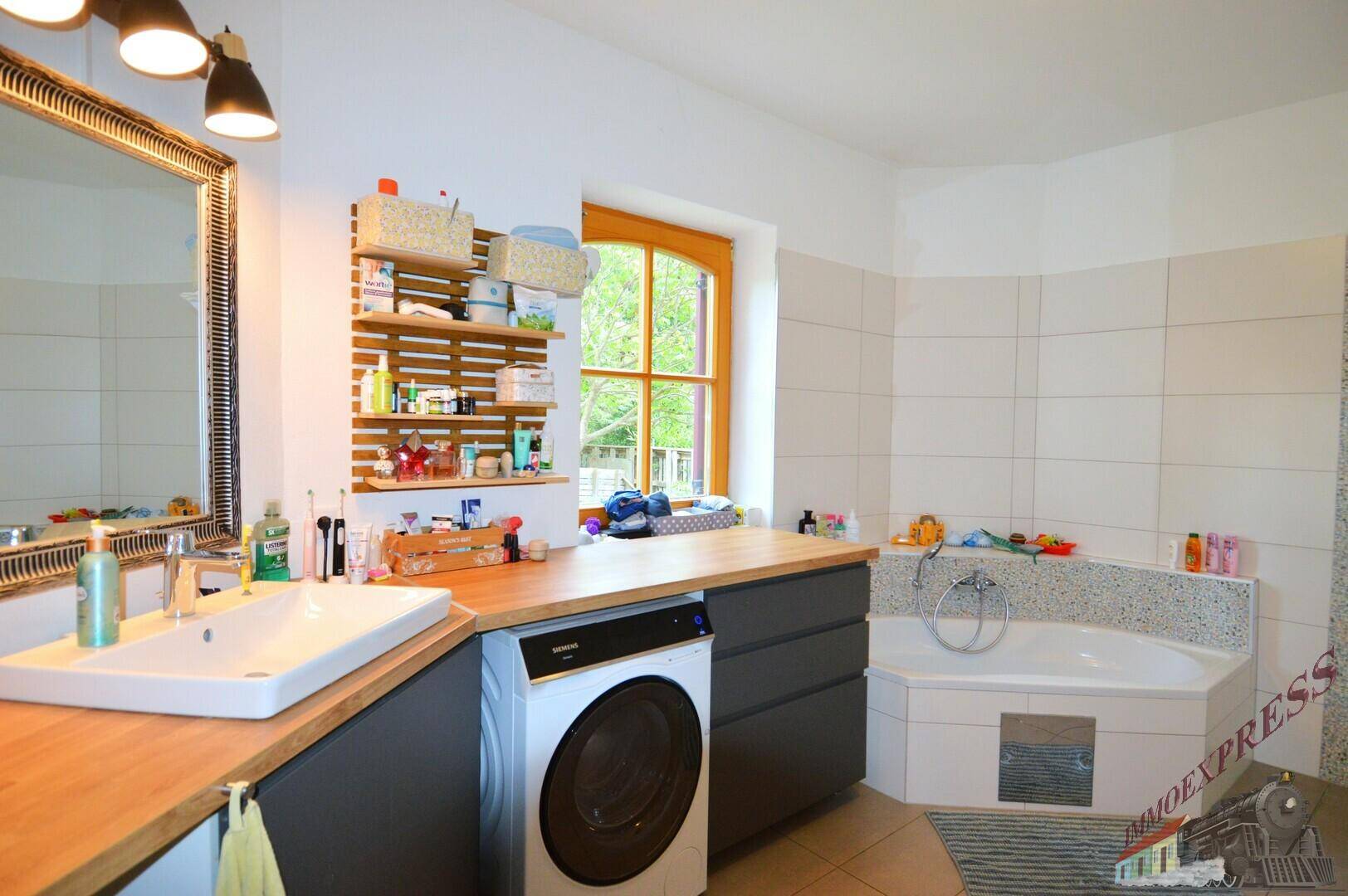 Geräumiges Badezimmer mit Eckbadewanne, Waschmaschine und Holzwaschtisch unter einem Fenster.