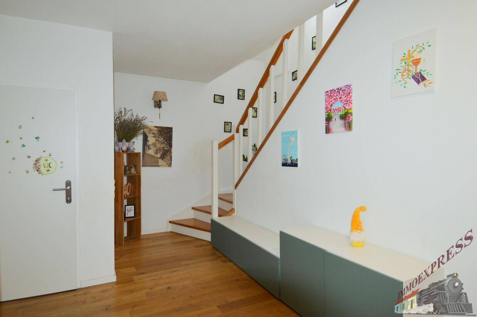 Heller Flur mit Holztreppe und dekorativen Bildern an der Wand, einladend und freundlich.