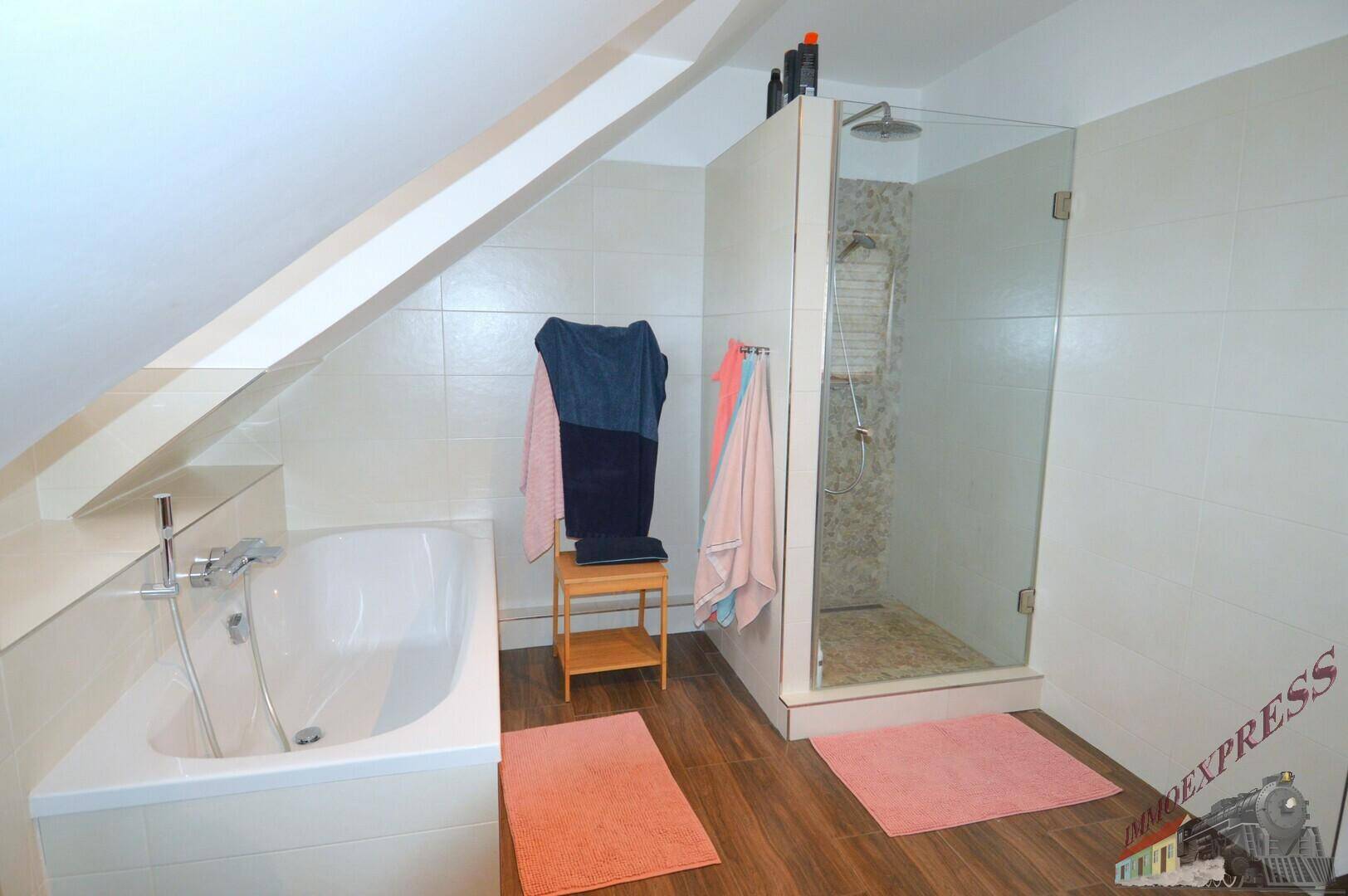 Helles Badezimmer im Dachgeschoss mit Badewanne, Glasdusche und Holzboden.