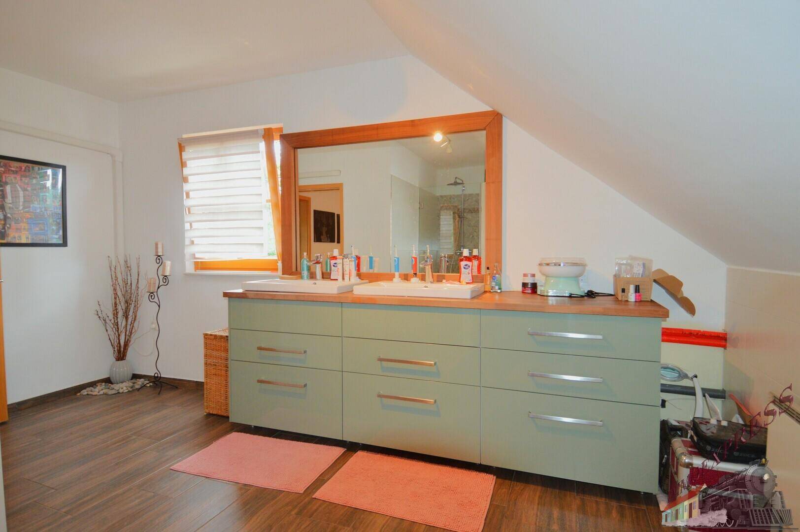 Geräumiges Badezimmer im Dachgeschoss mit Doppelwaschbecken, großem Spiegel und Holzboden.
