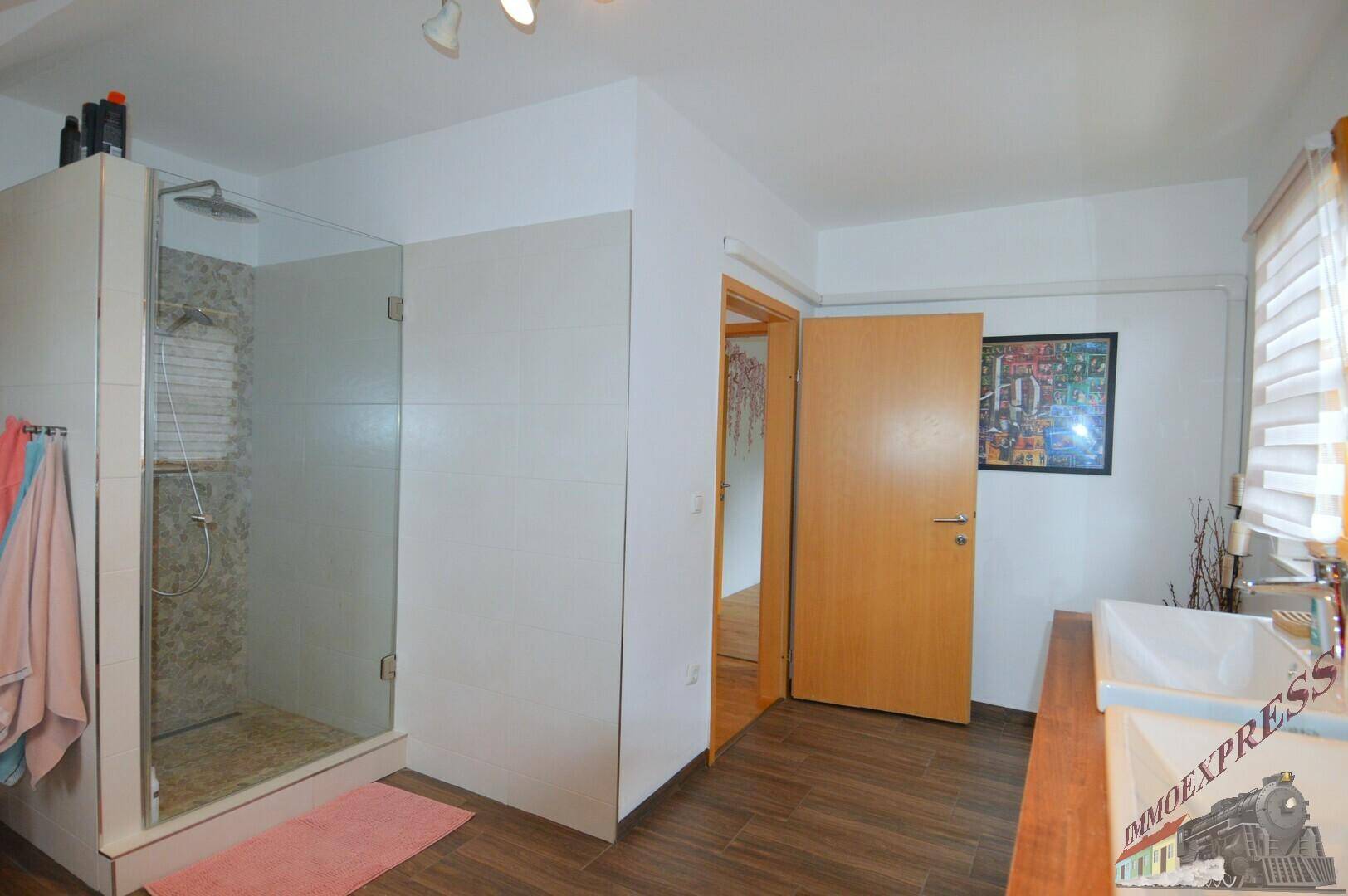 Modernes Badezimmer mit großer Glasdusche und Holzboden, angrenzend an einen Flur.