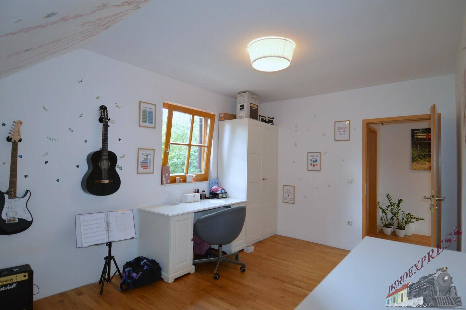 Kinderzimmer mit Schreibtisch, Gitarren an der Wand und Fenster mit Blick ins Grüne.