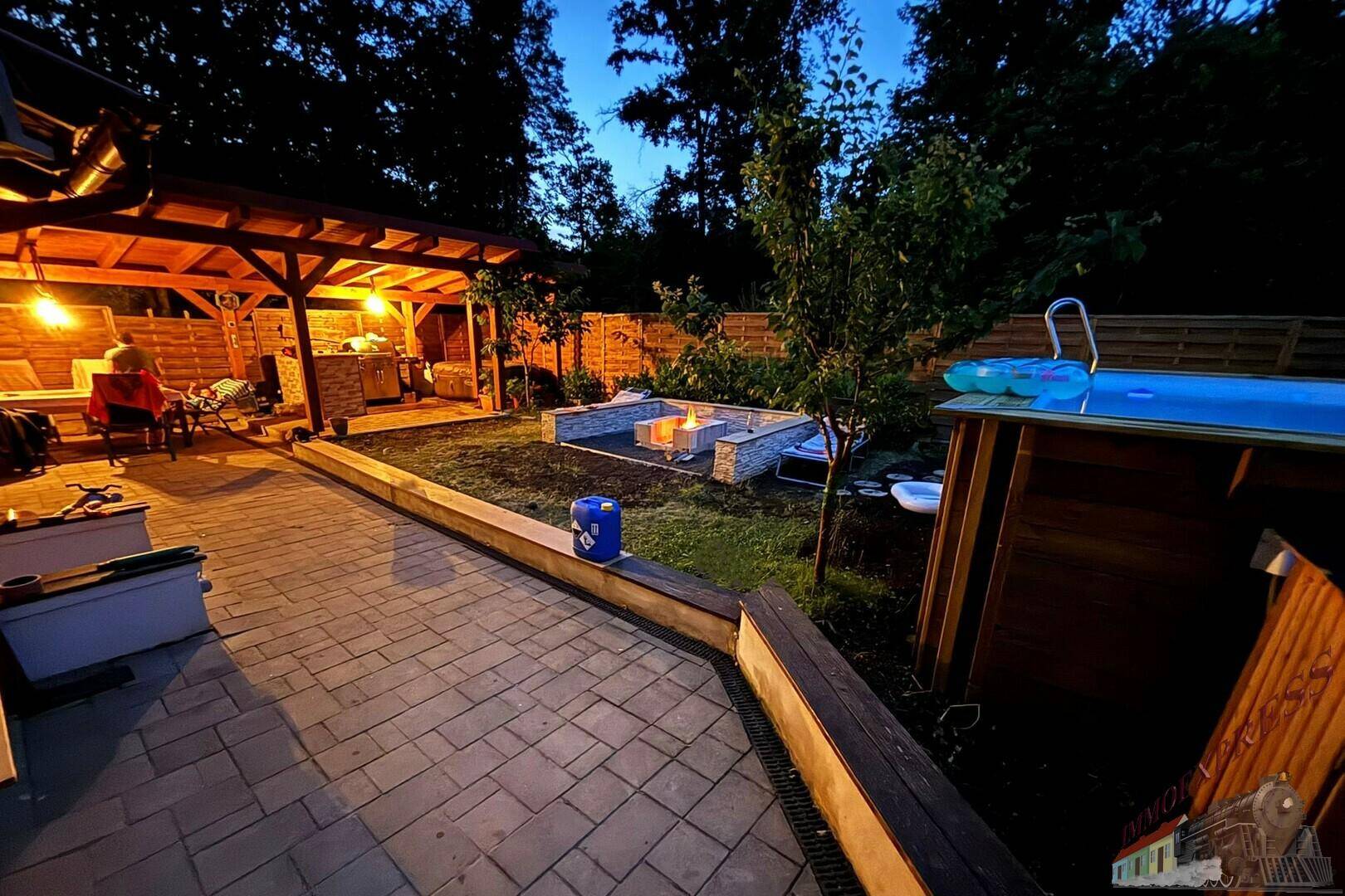 Beleuchteter Gartenbereich bei Nacht mit gemütlicher Feuerstelle, Pool und überdachter Terrasse.