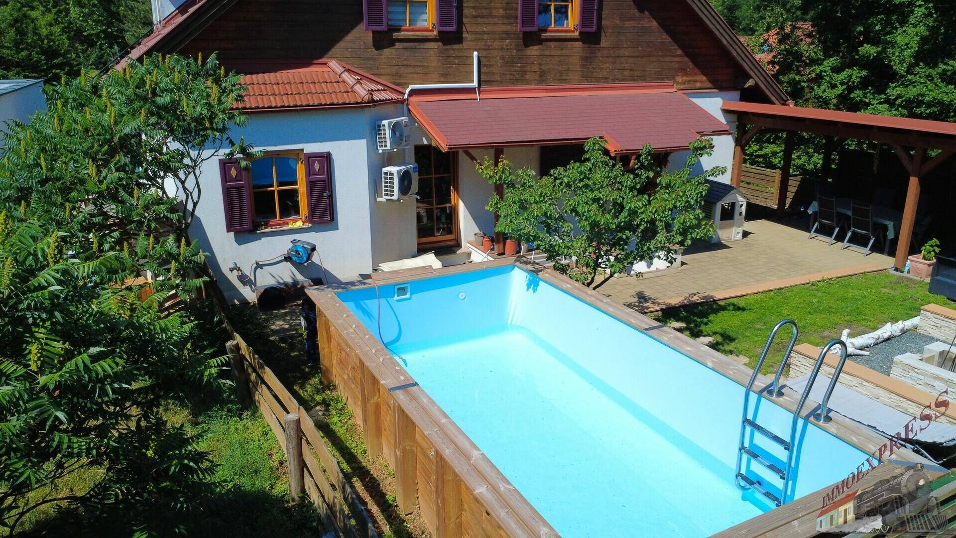 Hausfassade mit Außenpool und gepflegtem Gartenbereich unter blauem Himmel.