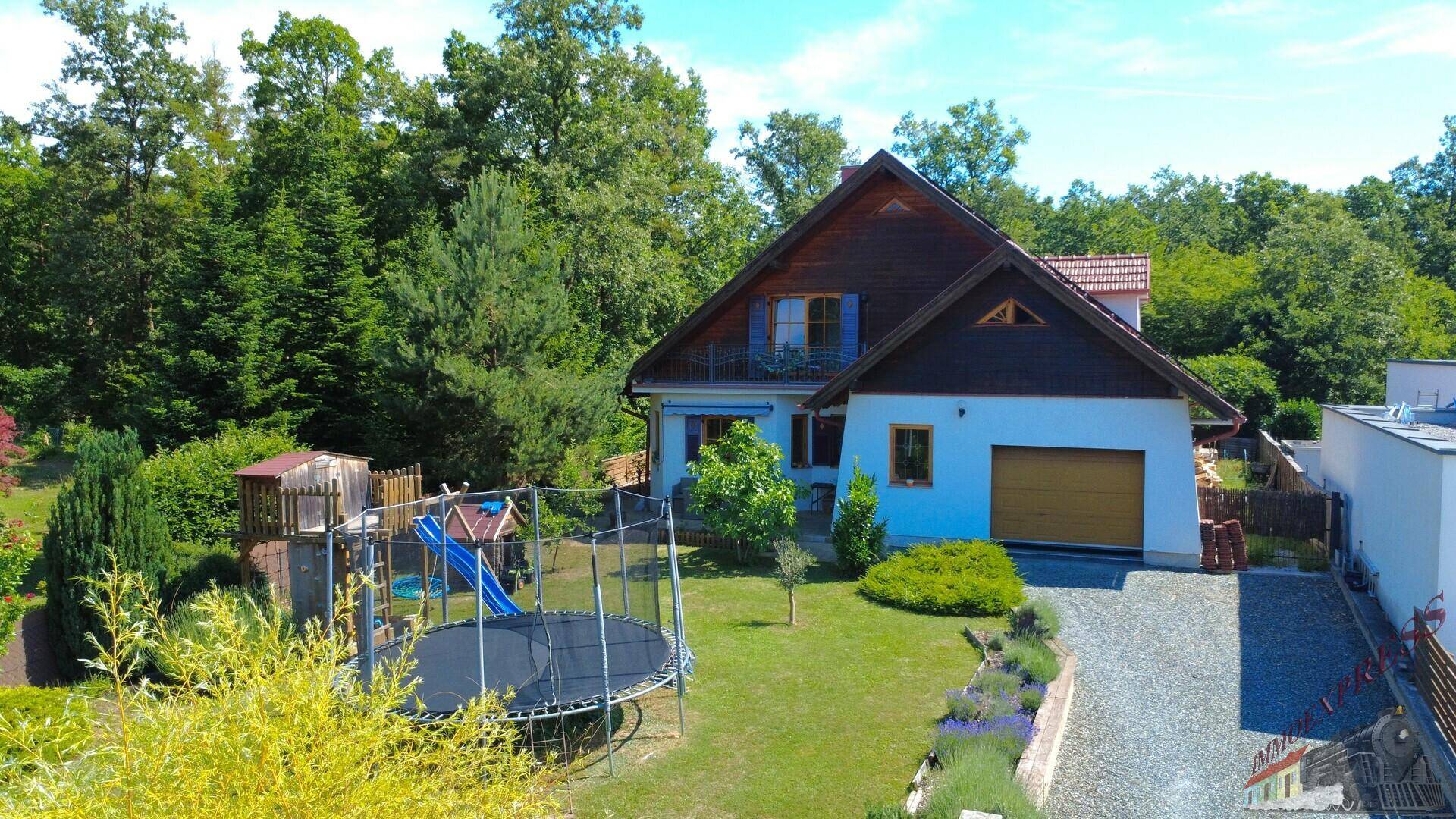 Rückansicht des Hauses mit großem Garten, Trampolin, Spielplatz und gepflasterter Auffahrt.