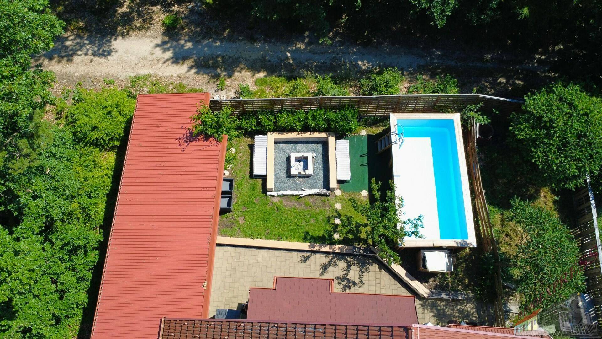 Luftaufnahme des hinteren Gartenbereichs mit Pool, Feuerstelle und Liegeflächen umgeben von Bäumen.