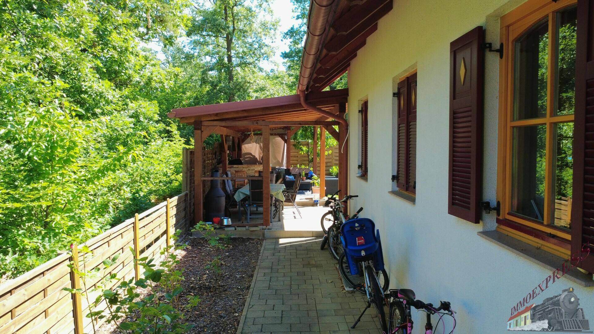 Überdachte Terrasse mit Holzbalken und Zugang zum Garten.