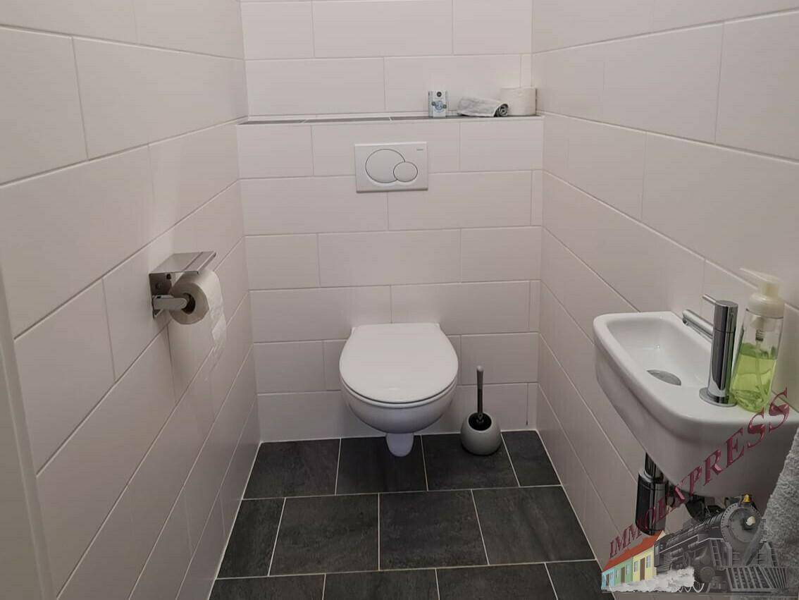 Modernes Gäste-WC mit wandhängendem WC, kleinem Waschbecken und dunklen Bodenfliesen.