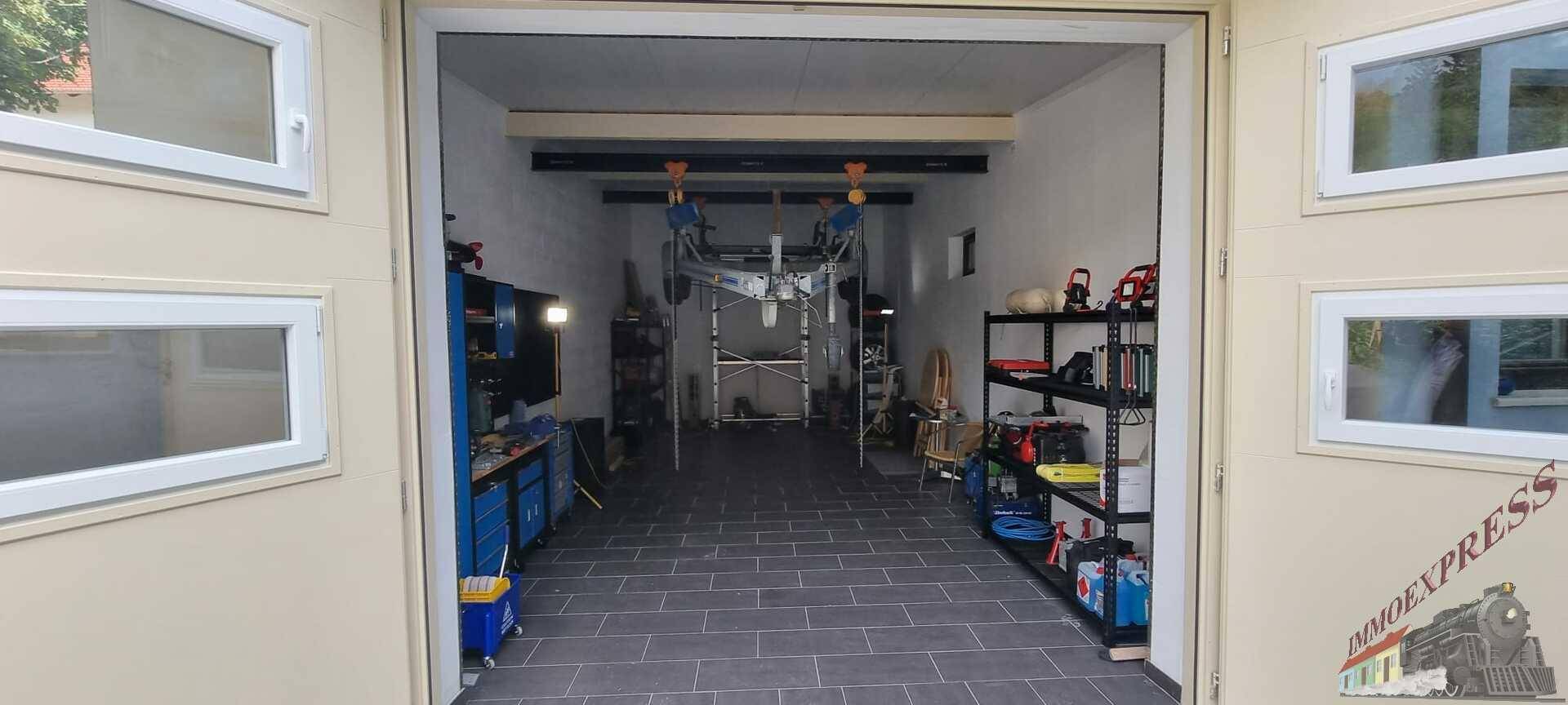 Geräumige Garage mit Werkstattbereich, Regalen und Fliesenboden.