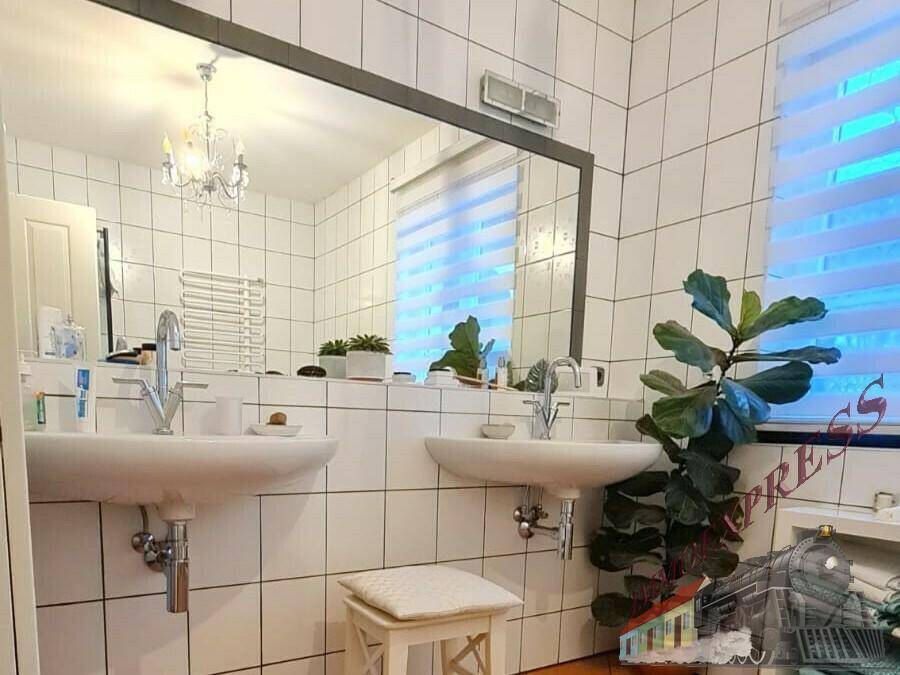 Helles Badezimmer mit Doppelwaschbecken, großem Spiegel und weißen Fliesen.