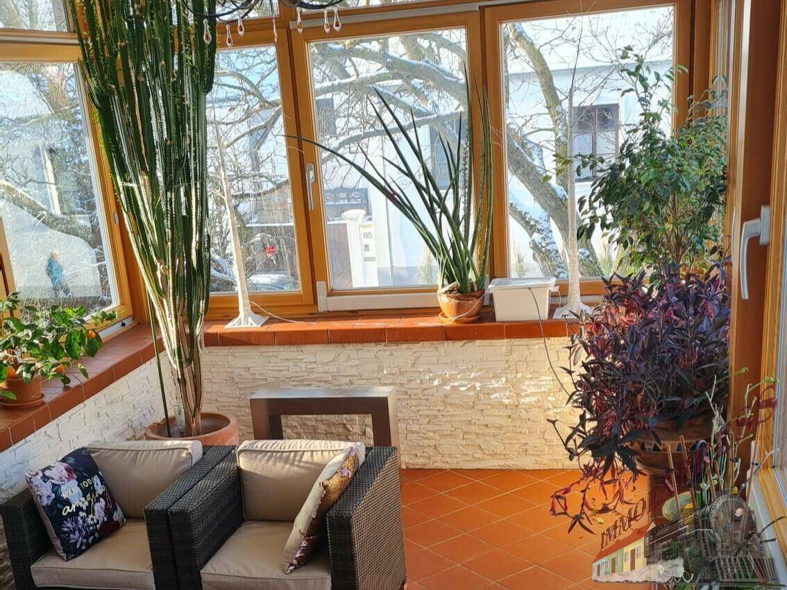 Heller Wintergarten mit vielen Pflanzen, gemütlichen Sitzgelegenheiten und Terracotta-Boden.