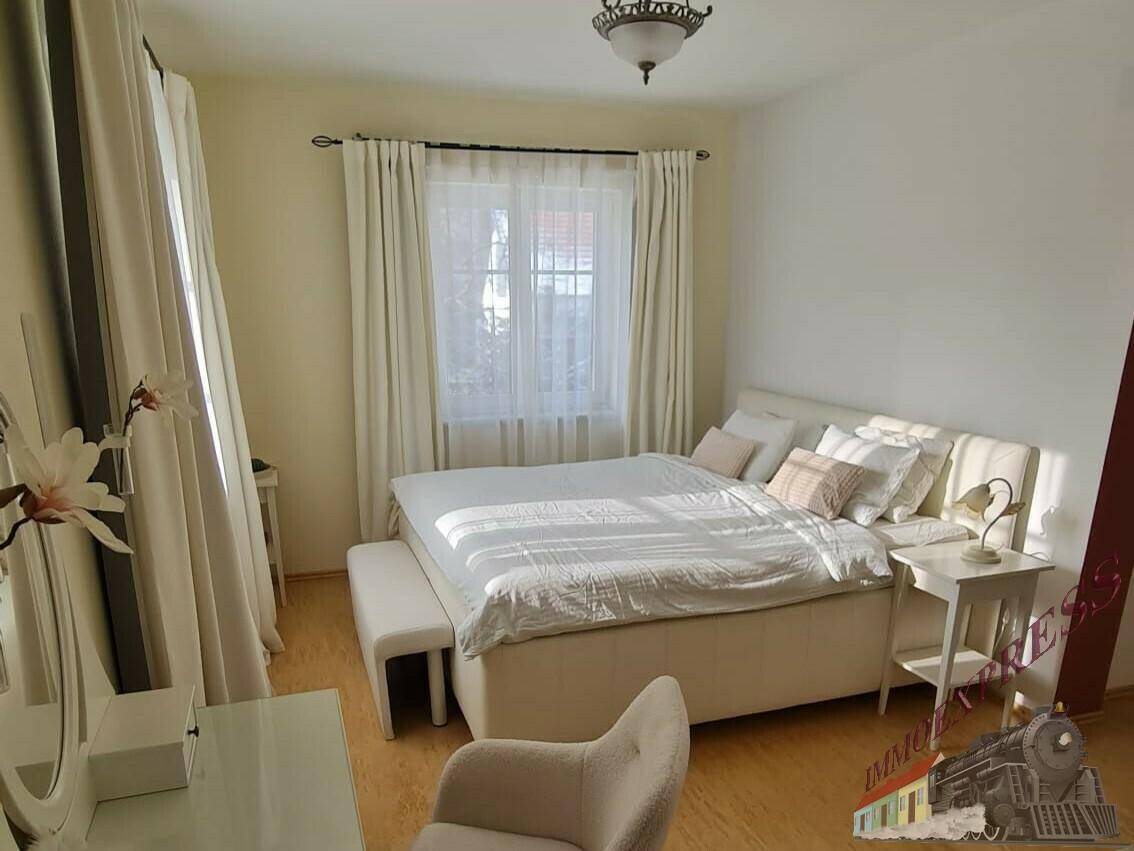 Helles Schlafzimmer mit Doppelbett, Nachttischen und großen Fenstern mit Vorhängen.