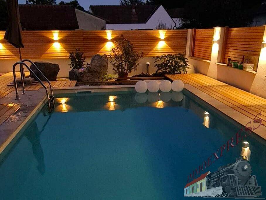 Beleuchteter Poolbereich bei Nacht mit Holzdeck und stimmungsvoller Außenbeleuchtung.