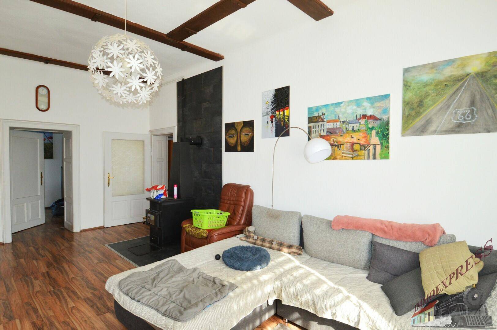 Geräumiges Wohnzimmer mit Kaminofen, großem Sofa und Holzbalken an der Decke.