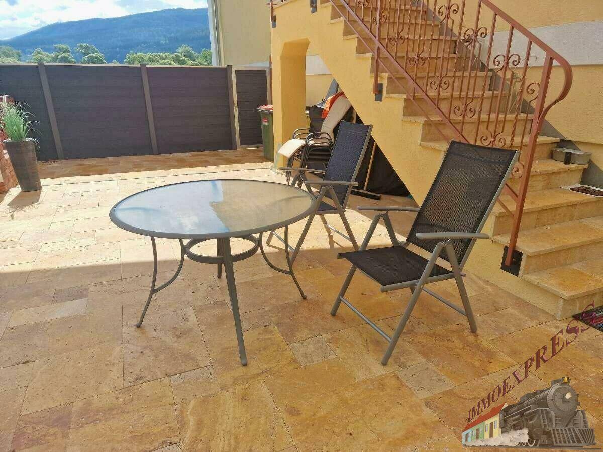 Möblierte Terrasse mit Steinfliesen und einem Tisch-Stuhl-Set, neben einer Außentreppe.