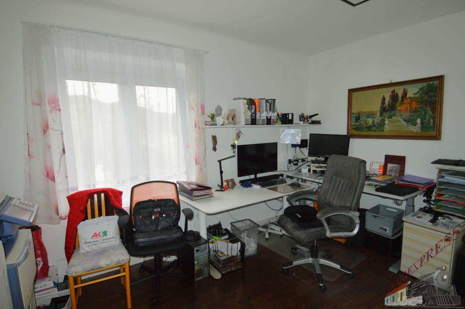 Funktionales Büro mit Schreibtisch, Computern und einem großen Fenster für viel Licht.