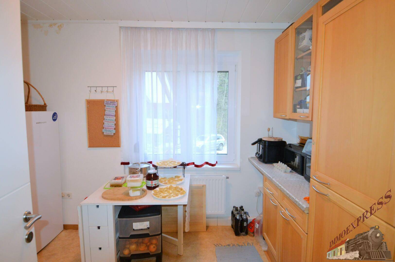 Kleine Küche mit Holzschränken, Arbeitsplatte und einem Fenster mit Blick nach draußen.