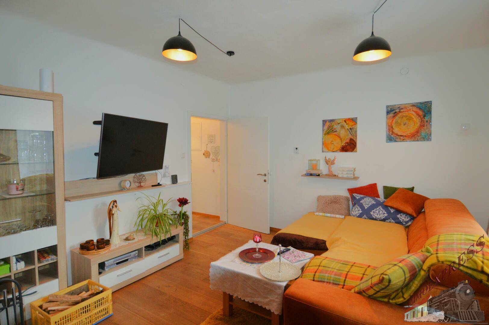 Gemütliches Wohnzimmer mit Sofa, Fernseher und Zugang zu einem weiteren Raum.