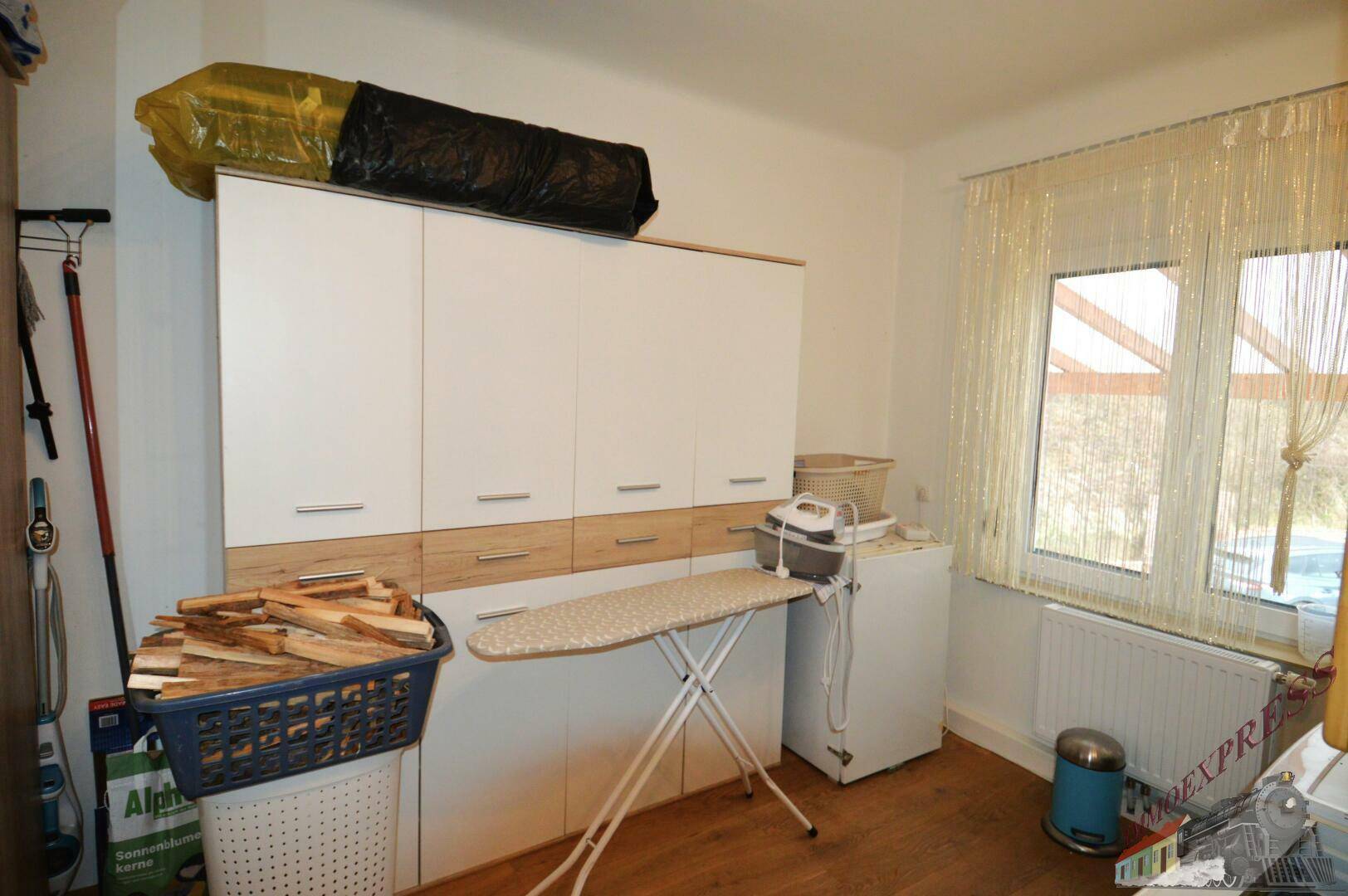 Geräumiger Hauswirtschaftsraum mit Schränken, Bügelbrett und Fenster für Tageslicht.