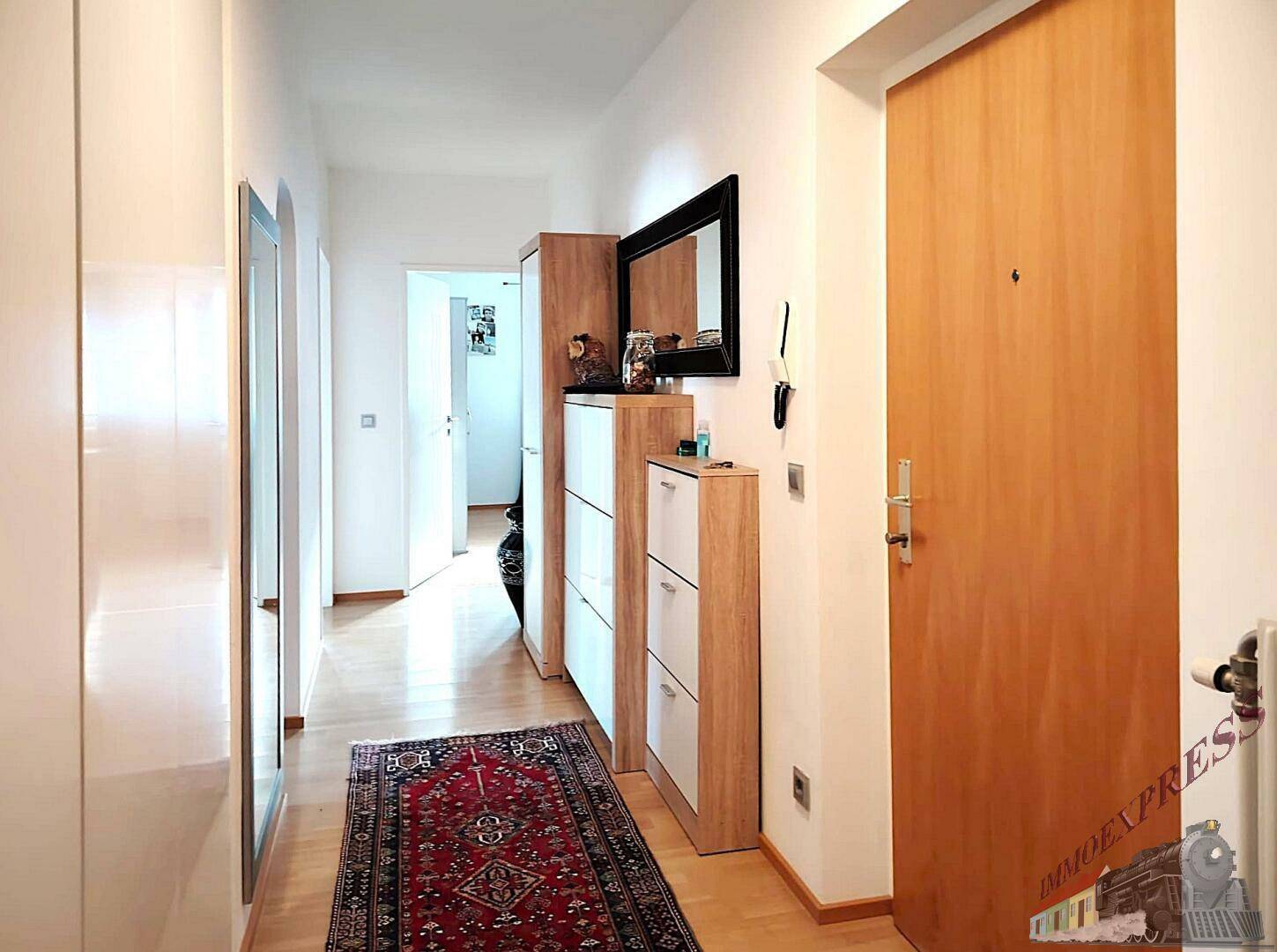 Heller Flur mit Holztür, praktischen Schuhschränken und einem großen Spiegel.