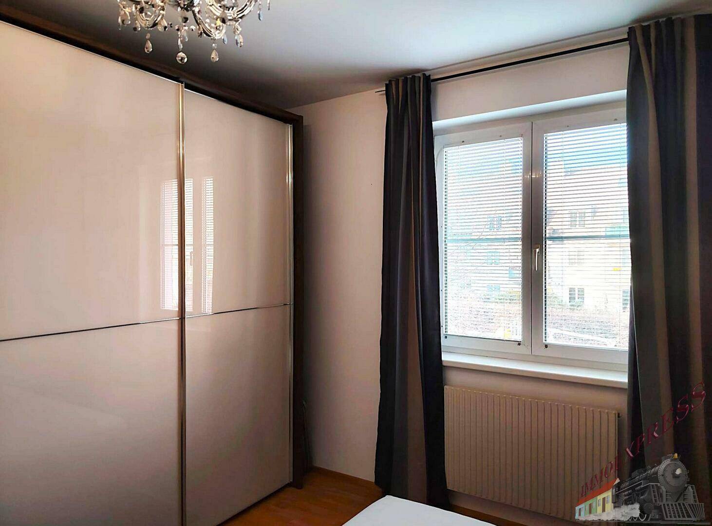 Schlafzimmer mit großem weißen Kleiderschrank und Fenster mit dunklen Vorhängen.