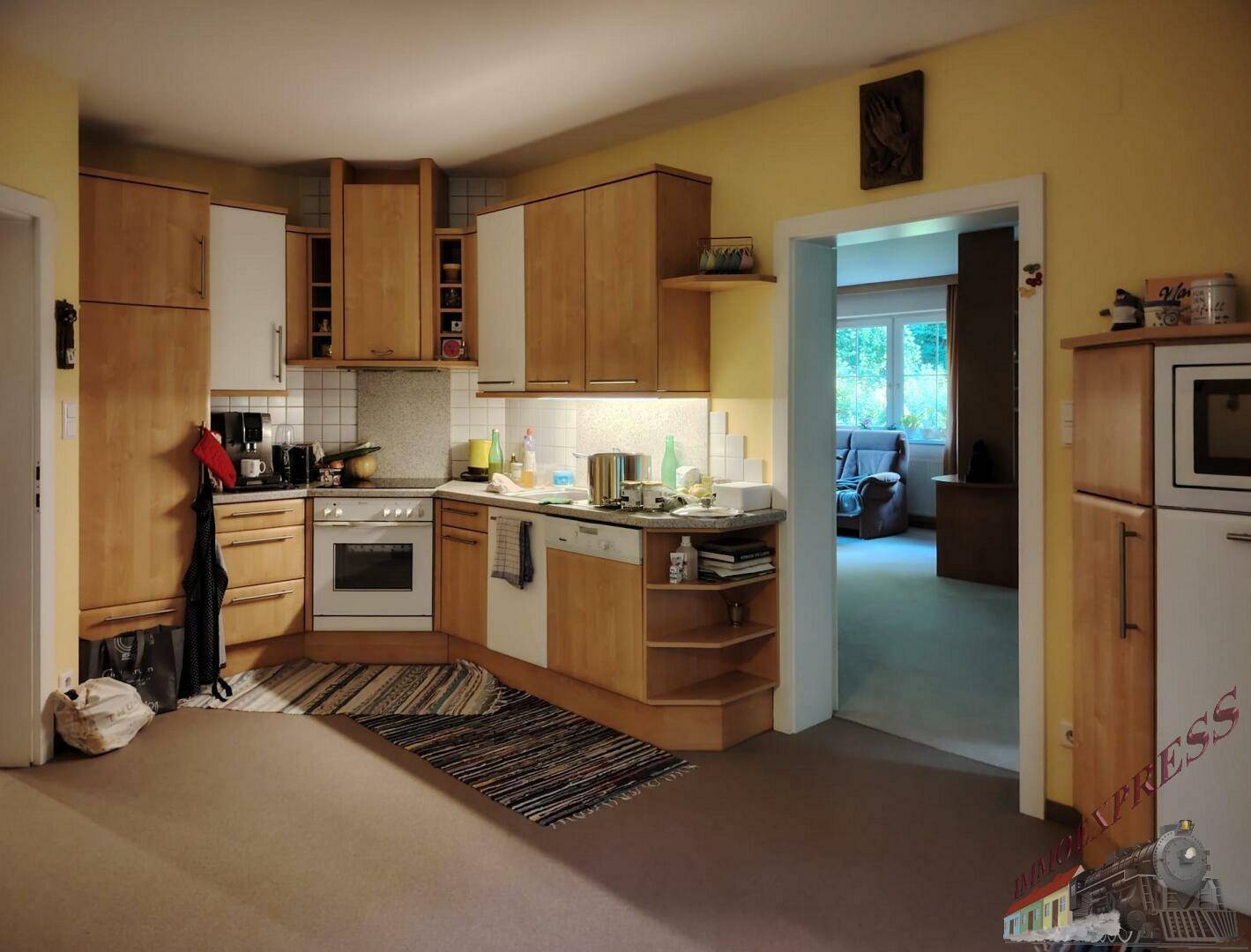 Funktionale Küche mit Holzfronten, hellen Arbeitsplatten und Blick in einen angrenzenden Wohnbereich.