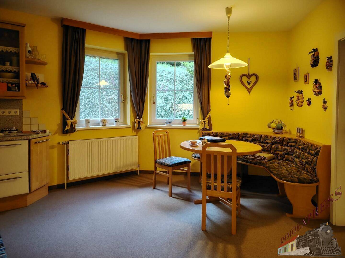 Gemütliche Wohnküche mit Eckbank, Esstisch und Fenstern, die viel Tageslicht hereinlassen.