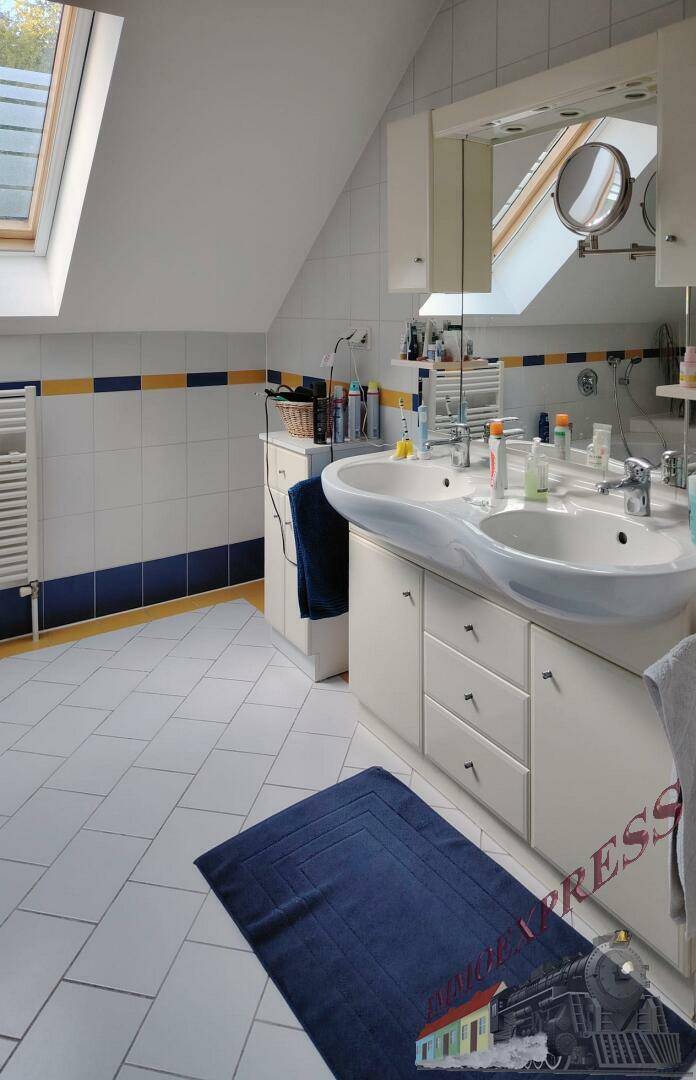 Badezimmer im Dachgeschoss mit Doppelwaschbecken, Spiegelschrank und Dachfenster für Tageslicht.