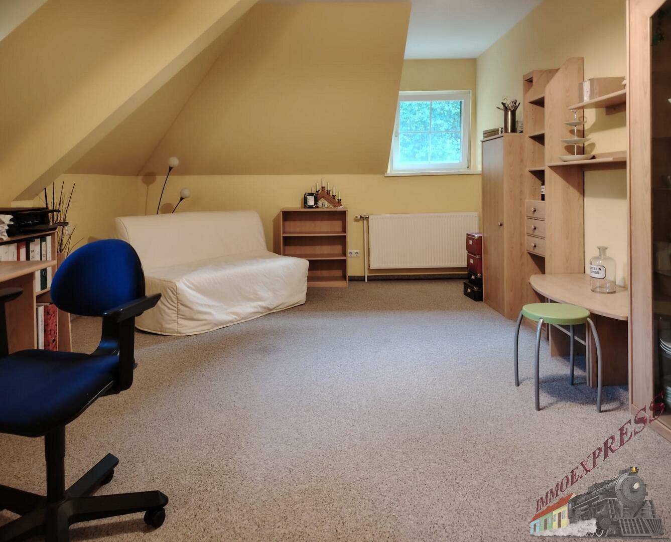 Vielseitig nutzbarer Raum im Dachgeschoss mit Schreibtisch, Sofa und Teppichboden.