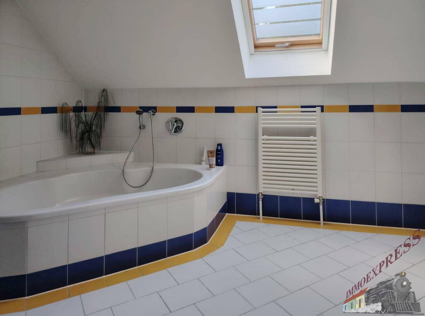 Geräumiges Badezimmer im Dachgeschoss mit Eckbadewanne, Dachfenster und farbigen Fliesen.