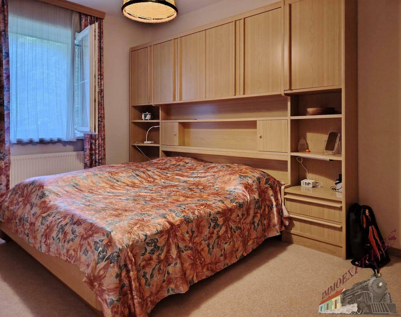 Schlafzimmer mit großem Doppelbett, integrierten Schränken und einem Fenster mit Blick ins Grüne.