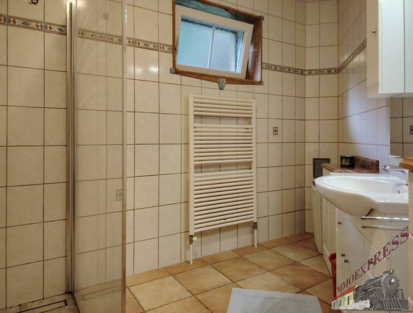 Badezimmer mit beigefarbenen Fliesen, Duschkabine, Waschbecken und beheiztem Handtuchhalter.
